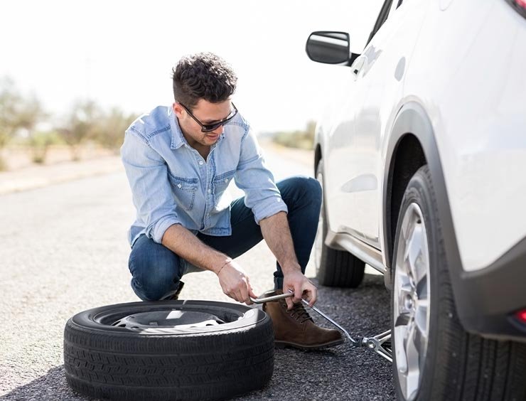 Automobilista in sosta per cambiare pneumatico forato. Il lad...